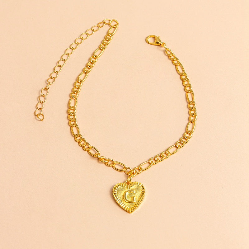 Gold bracelet with a heart-shaped charm letter G on a beige background