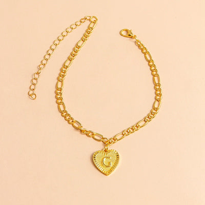 Gold bracelet with a heart-shaped charm letter G on a beige background
