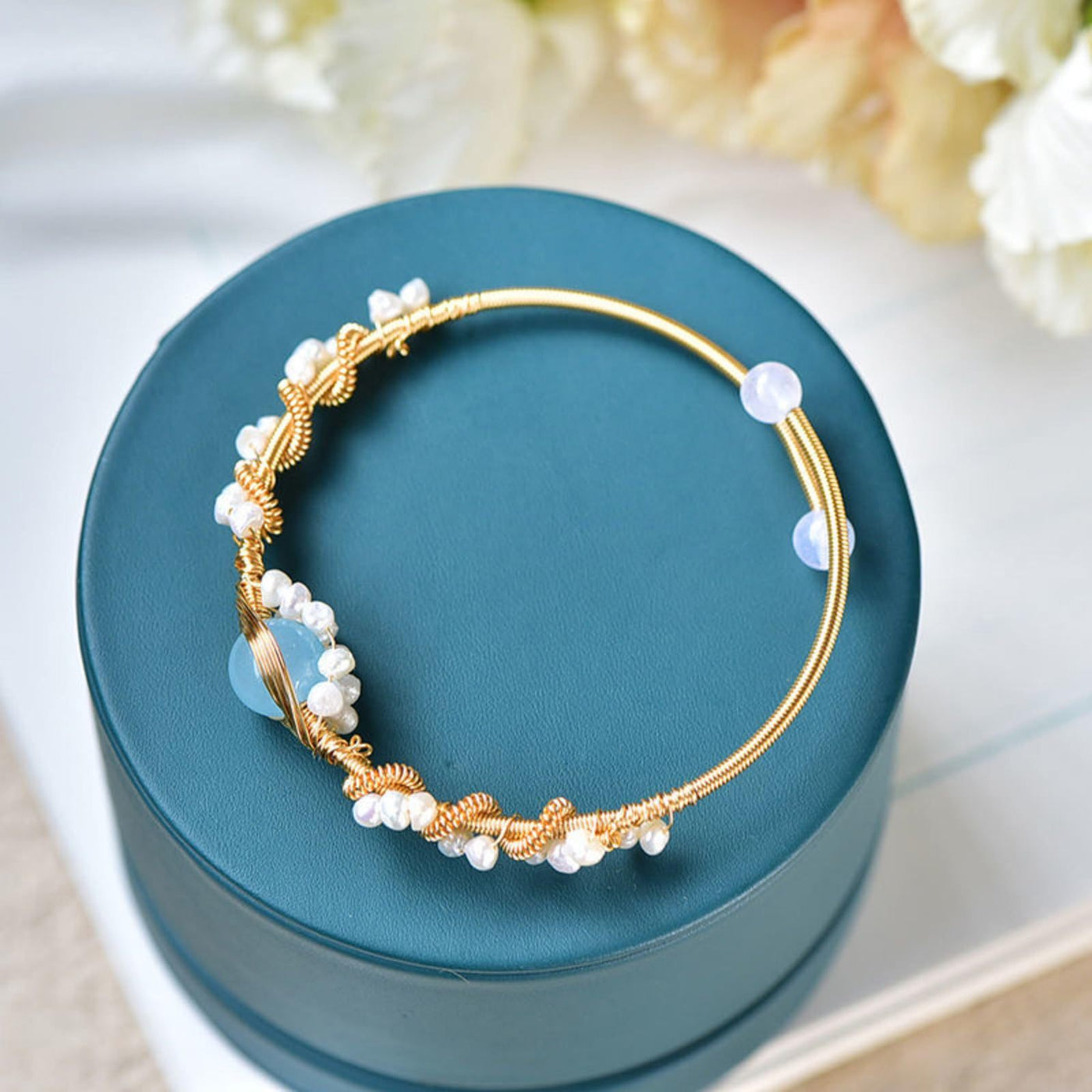 Gold bracelet with pearls on a teal box with flowers in the background