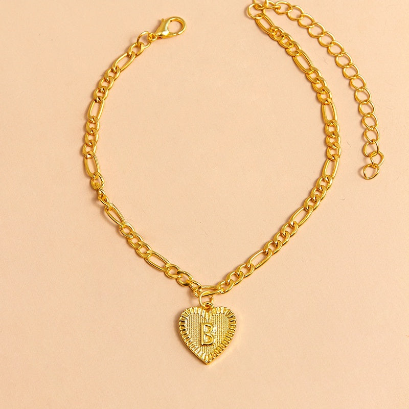Gold chain bracelet with a heart-shaped charm letter B on a beige background
