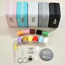 Set of sewing supplies including spools of thread, scissors, and a needle case on a light background.