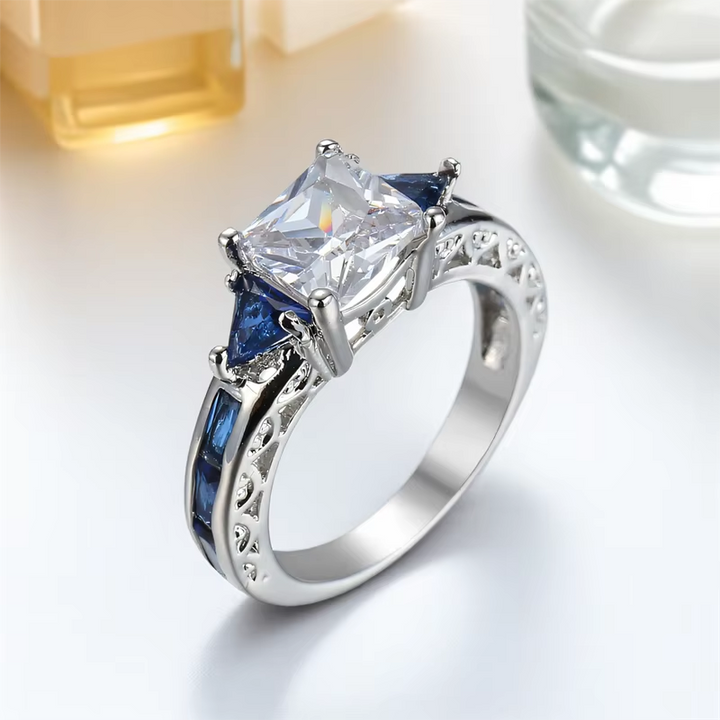 Silver ring with a large central gemstone and smaller blue stones on a light background