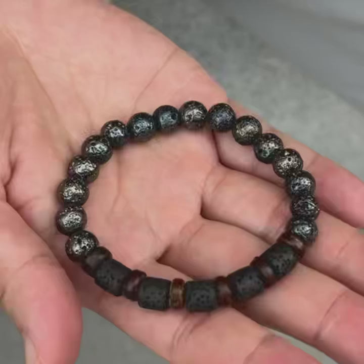 video demonstrating Black beaded bracelet with brown and gold accents held in hands on a textured surface