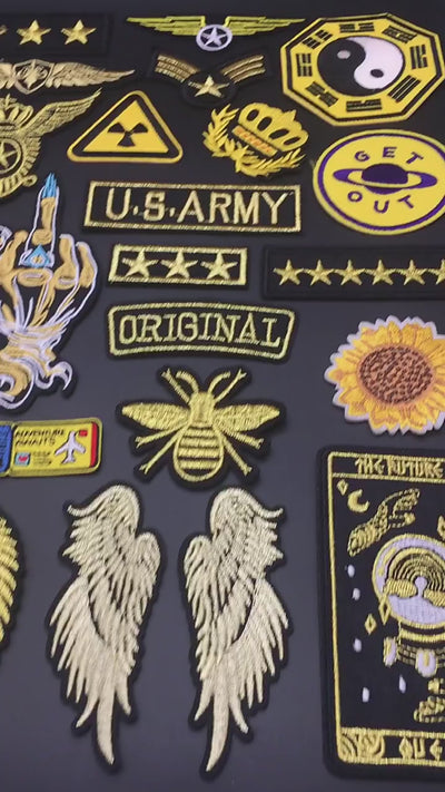 video of Embroidered golden wings and badge patch with military, cosmic, and crown symbols on black background