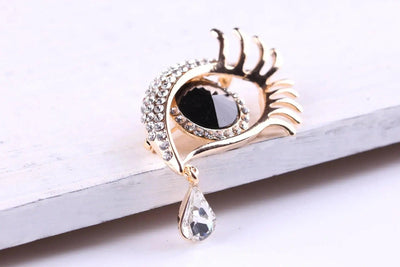 BROOCHITON Brooches diamond-encrusted tear eye design brooch gold and white  flat on white surface
